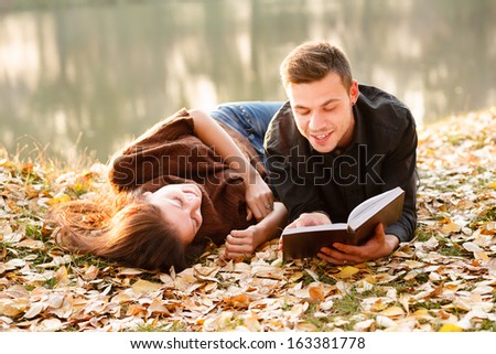 young man lying down near lake reading to his girlfriend
