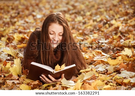 young female lying down on autumn leaves reading book