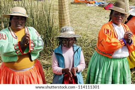 PUNO, PERU - JULY 28: Women and unidentified child in traditional dresses sing to welcome tourists in Uros Island, city of Puno, Peru, July 28. 2012.