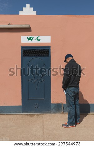 The asian man play mobile phone during waiting for toilet at gas station in Merzouga city, Morocco