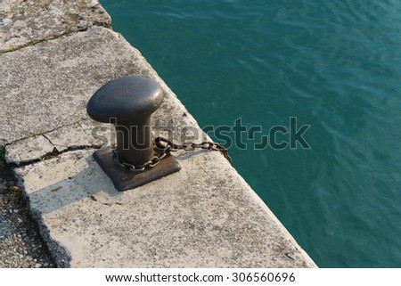 Metal bollard and chain on a quay or wharf at a docks or harbour for mooring boats and ships, close up view