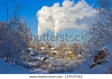 Village houses in the winter in the snow against the blue sky and the thick smoke from factory chimneys
