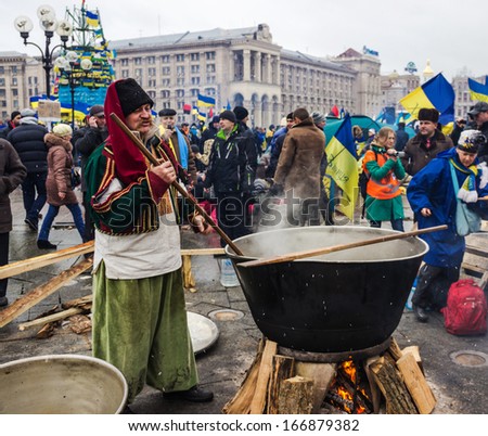 KIEV, UKRAINE - DEC 8, 2013. Elderly man in national dress Cossack prepares food in a large cauldron to people protesting on the Maidan in Kiev.