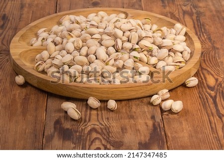 Heap of the roasted salted pistachio nuts with partly open shells on a wooden compartmental dish on the old rustic table, side view close-up in selective focus 商業照片 © 