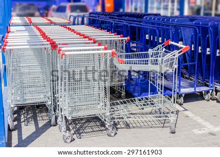 Rows of ordinary shopping baskets and trolleys for heavy building materials in the parking lot near the supermarket building