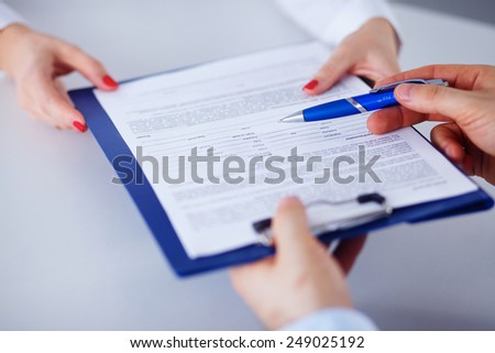 Business colleagues sitting together at table and viewing documents from clipboard
