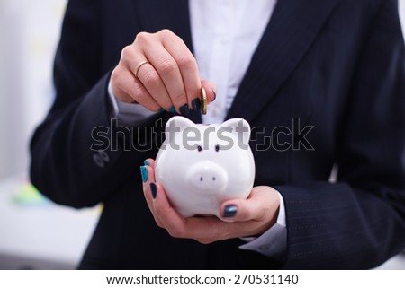 Businesswoman putting  money into a piggy bank isolated on white background