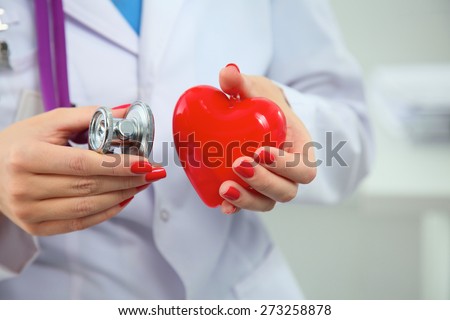 Young woman doctor holding a red heart, isolated on white background