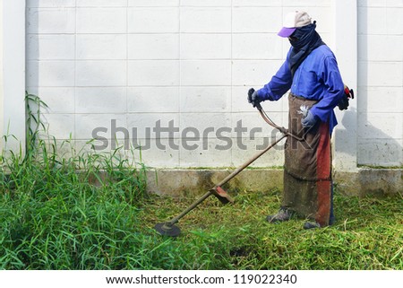Worker mowing weed near the fence with mowing machine