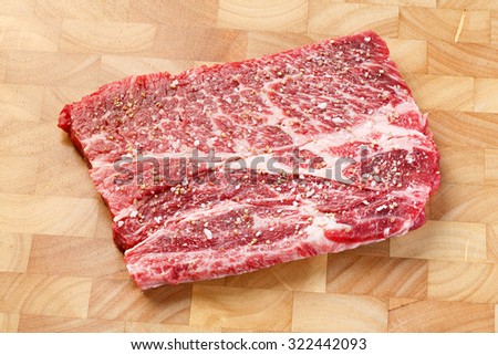 Close up beef chuck steak with sea salt and pepper on wooden chopping board, deep focus image