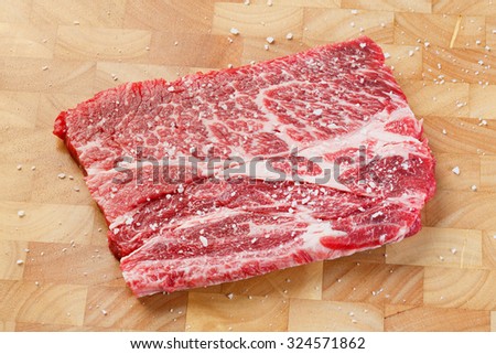Close up beef chuck steak with sea salt on wooden chopping board, deep focus image