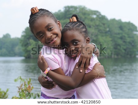 close sisters - two cute schoolgirls hugging by a lake