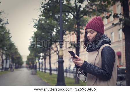 Beautiful young girl listens to music, reads and writes in the smart phone in the center of St. Petersburg