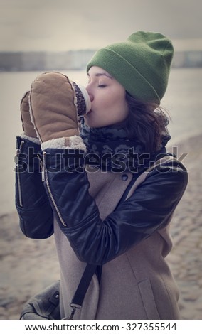 Beautiful young girl in a leather jacket with a cup of hot coffee in the city of St. Petersburg