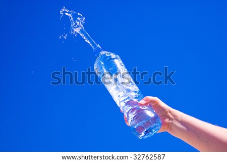 Pure water splashing from bottle against blue sky