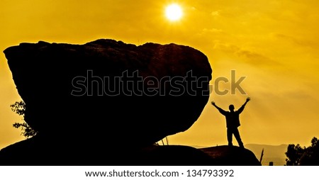 Praying man silhouette on sunrire background with big stone