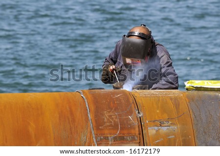 Worker welding two big pipes in a harbour