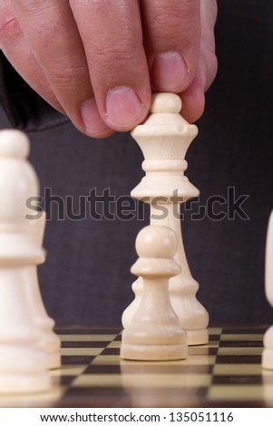 Businessman playing chess and holding queen chess piece.