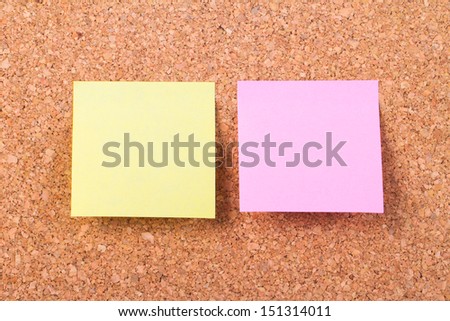 Blank, empty, yellow and pink sticky post it notes on cork bulletin board.