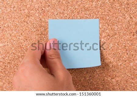 Hand and blank, blue sticky post it note for your message on cork bulletin board.