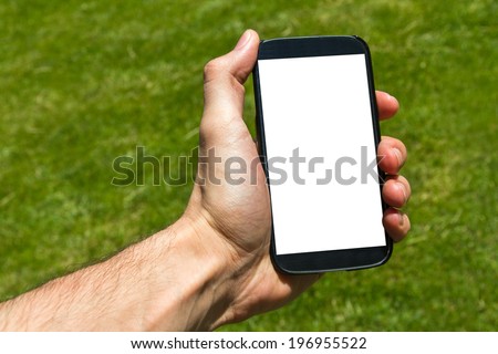 Young male hand holding and showing smart phone with blank white screen on green background filled grass.