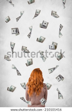 Young red head woman standing and one hundred dollar banknotes flowing around, back view, isolated on white, grunge background.