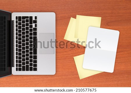 Laptop and yellow sticky posts and white, blank note book on modern, wooden office table.