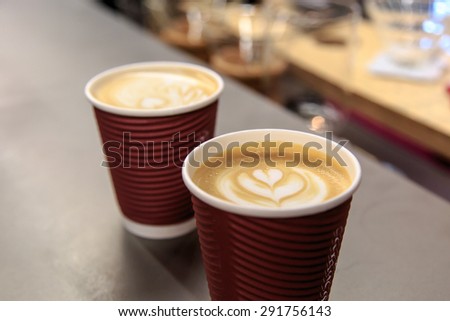 Side view of two latte art coffees with heart figure on, in take away paper glass in a cafe.