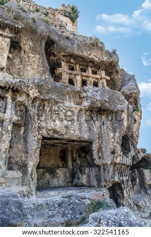 View of abandoned and destroyed rock tombs of Tlos Ancient City, on cloudy blue sky background.