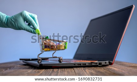 A hand in a sterile medical glove holds a shopping cart with a credit card for online purchases. Concept of internet purchasing important life support products during the coronavirus pandemic