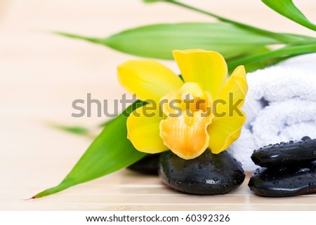 Yellow orchid, spa stones, towel and bamboo leaves on bamboo mat for spa concept