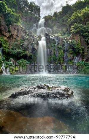 Moving water at the beautiful Trois Bassins waterfall as it plunges into a blue lagoon on Reunion Island.