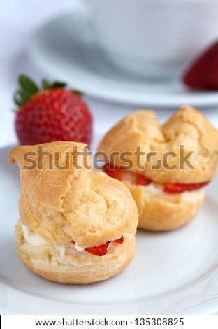 Fresh cream puff with whipped cream and strawberries on white plate on white wooden table, close up