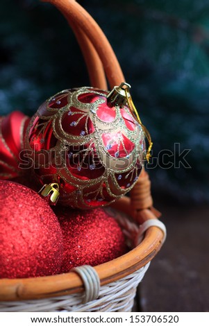 Christmas decoration, red glass balls in a wicker basket on a wooden table. Christmas tree in the background. Selective focus on one of the balls.
