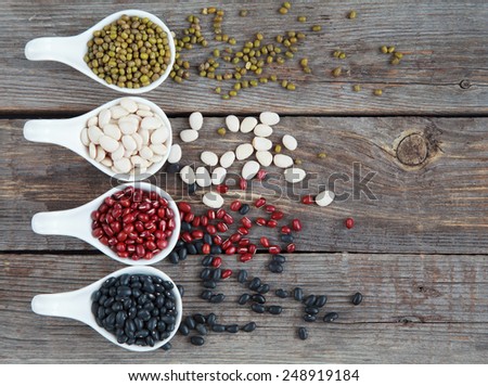 Set of different varieties of beans: baby lima, black small, adzuki and  mung in white ceramic spoons (appetizers) on wooden background, selective focus on beans
