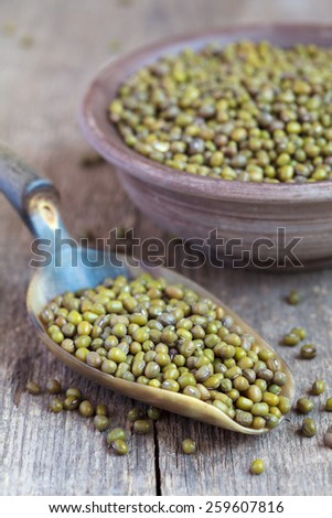 Dry green Mung beans in a clay bowl and in the scoop on wooden table, selective focus - some beans in focus, some are not