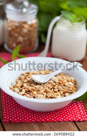 Breakfast: homemade granola in a white plate, yogurt with jam and a jug of milk on a wooden table. Selective focus.
