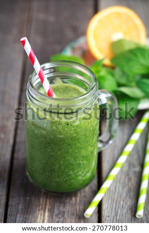 Healthy green smoothie made from spinach, kiwi, bananas and oranges in a jar with red straw on a wooden table, selective focus