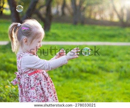 Little blond girl catching soap bubbles. Selective focus and space for text