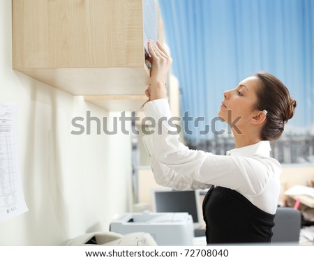 Office life. Woman searches for documents on a shelf. Focusrd on left hand.