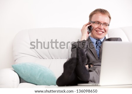 Young handsome man in suit sitting on sofa and talking on phone smiling in living room