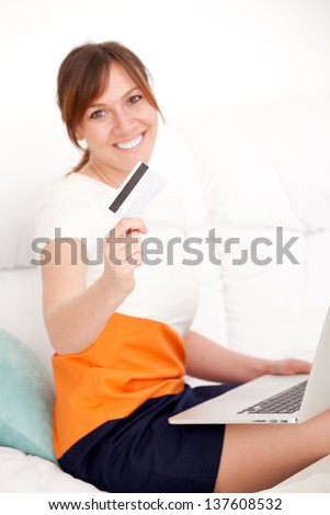 charming woman with card in hand sitting on sofa in living room looking into camera