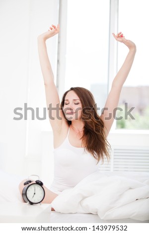 Tired sleepy woman waking up and giving a stretch while sitting in bed at home