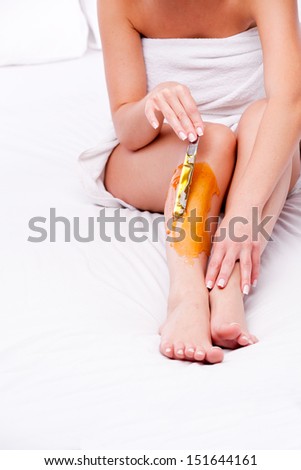 applying wax to females leg to remove hair over white