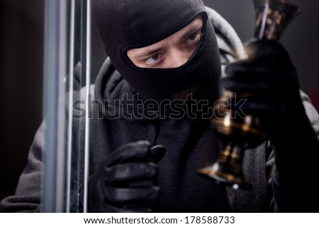 Angry burglar wearing black woollen mask, considering vase over black