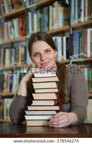 Portrait of beautiful student girl sitting at desk in Begen city library with a pile of books and looking at camera