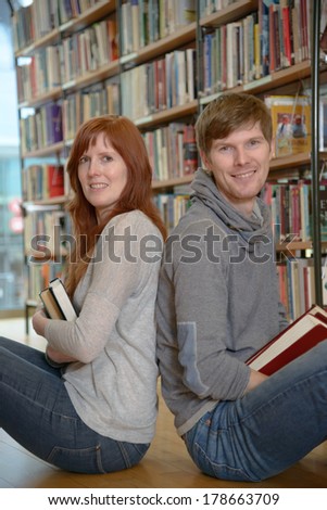 Two young university students sitting back to back in a library and ?miling at camera