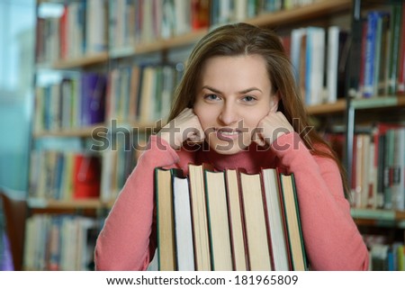 Portrait of beautiful student girl sitting at desk in Bergen city library with a pile of books and looking at camera