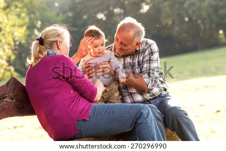 Grandparents with grandson enjoying the sunny autumn day in park.