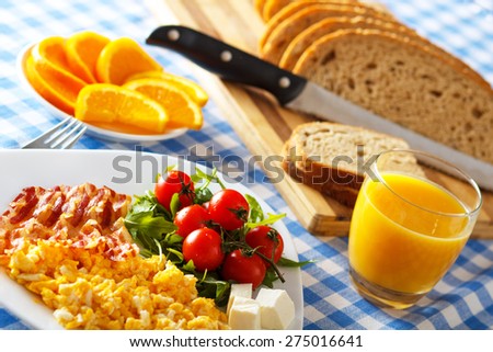 Closeup of a breakfast table with bacon, scrambled eggs, fruit and orange juice.
